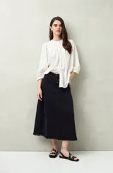Falda midi de denim negro con tiro bajo, corte evasé, costuras verticales y ruedo desflecado.
