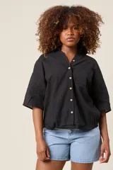 Camisa color beige claro, de corte clásico, con cuello, botones frontales, bolsillo en el pecho y mangas tres cuartos con presilla para sujetar.