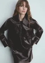 Chaqueta corta de poliuretano color marrón oscuro con textura, cuello camisero, manga larga con puños abotonados, dos bolsillos de solapa en la parte delantera y cierre frontal con botones.