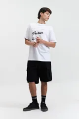 Remera blanca de manga corta con estampado frontal que incluye la palabra 'Savior' en letras cursivas negras y otros textos en tipografía sans-serif. Corte regular.