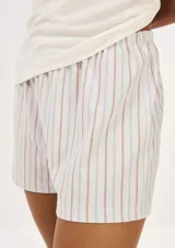 Pijama de dos piezas compuesto por una remera de manga corta color crema con un pequeño bordado de concha marina y un short de tiro alto con elástico y estampado de cuadrícula en tonos beige y blanco.