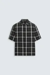 Camisa de hombre relaxed fit con estampado de cuadros blancos sobre fondo negro, cuello solapa, manga corta y cierre frontal con botones.