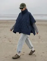 Poncho acolchado color azul marino, con cuello alto y cierre frontal. Presenta un patrón de costuras onduladas y mangas cortas tipo capa.