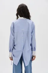 Camisa a rayas de 100% algodón con cuello blanco, puños innovadores, jaretas con lazos en los laterales y bolsa con botones en la espalda.