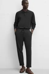 Pantalón negro de corte cropped, con cintura elástica ajustable con cordón, bolsillos laterales y traseros de vivo. El bajo tiene terminación con vuelta.