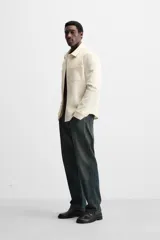 Sobrecamisa negra de tejido con elasticidad, cuello solapa y manga larga acabada en puño con botón a presión. Tiene bolsillos de plastrón en el pecho y cierre frontal con botones a presión.