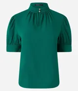 Blusa verde esmeralda de crepé con cuello alto, botones dobles y pequeña abertura en el cuello. Tiene mangas cortas abullonadas con botones.