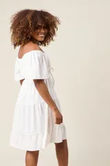 Vestido corto blanco con escote bardot, cintura fruncida y falda escalonada con vuelo.