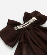 Accesorio para el pelo color marrón oscuro, con forma de lazo y caida de tejido. Modelo pinza.