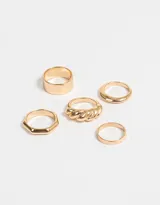 Set de cinco anillos dorados con diferentes diseños: uno liso delgado, uno facetado, uno ancho, uno con forma de soga trenzada y uno con forma de gota.