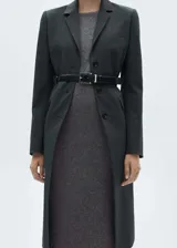 Vestido midi de punto color gris, con cuello barco, manga larga y corte entallado. Incluye cinturón de cuero negro con hebilla plateada.