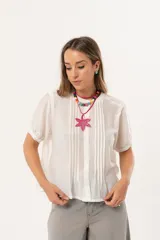 Blusa blanca de mangas cortas con cuello redondo y abotonadura frontal.