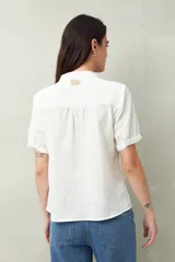 Camisa blanca de manga corta abullonada, cuello mao y botones forrados.