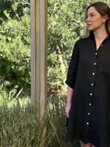 Vestido camisero blanco de lino, con cuello camisero, manga larga con botón para recoger, cierre frontal con botones de nácar, bolsillo en el pecho y diseño asimétrico más largo en la parte trasera.