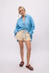 Camisa blanca de lino y algodón, con cuello clásico, cierre frontal con lazos y mangas largas abullonadas con puños ajustables con lazos.