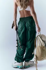 Pantalón cargo verde oscuro de nylon, con cintura elástica y cordón amarillo ajustable. Presenta detalles fruncidos en las piernas y bolsillos laterales.