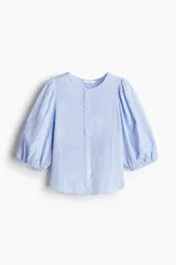 Blusa celeste y blanca a rayas verticales, de corte recto, con cuello redondo, cierre frontal con botones y mangas 3/4 abullonadas con puños elásticos.