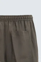 Pantalón de lino color marrón oscuro, de corte recto y relaxed fit. Tiene cintura elástica ajustable con cordón, bolsillos frontales y traseros de parche.