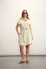 Vestido camisero corto color beige, con cuello clásico, mangas cortas con puños, dos bolsillos con solapa en el pecho, cinturón de lazo y cierre frontal con botones.