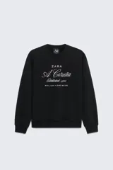 Sudadera negra de cuello redondo y manga larga, con bordado blanco en el frente que dice 'Zara A Coruña Established 1975 Rúa Juan Flórez 64-66' y un logo pequeño con el número 50 en la parte superior.