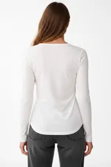 Remera de manga larga entallada en color blanco, confeccionada en algodón. Presenta cuello redondo con una hilera de botones frontales y un pequeño bolsillo en el pecho con detalle de botón.