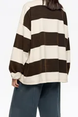 Camiseta de manga larga con corte oversize y escote redondo. Presenta un patrón de rayas horizontales anchas en color marrón oscuro y beige claro. Posee un pequeño logo bordado en la parte inferior derecha.