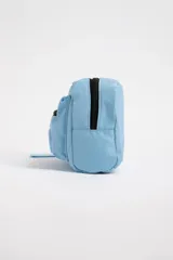 Necesser celeste rectangular de tela acolchada, con cierre superior y bolsillo frontal con cierre. Tiene una correa de mano en un lateral.