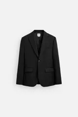 Blazer negro de lana con corte regular fit. Tiene cuello con solapas de muesca, manga larga con puños abotonados, bolsillos de vivo en pecho y de solapa en cadera, bolsillo interior, aberturas en la espalda y cierre frontal con botones.