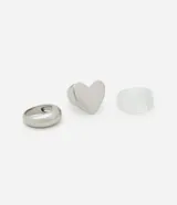 Set de tres anillos plateados y transparentes con diferentes diseños: uno liso, uno con forma de corazón y uno de resina transparente.