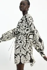 Vestido corto en mezcla de viscosa con estampado floral en blanco y negro, cuello mao fruncido y abertura en V adelante. Modelo de corte holgado con cinturón extraíble para atar en la cintura, y mangas globo largas de corte raglán con abertura y botón en los puños.