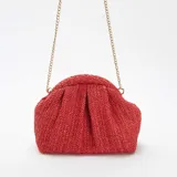 Bolso de mano tipo clutch, color rojo, confeccionado en rafia trenzada. Tiene forma rectangular con pliegues en la parte superior y cierre con broche imantado. Incluye una cadena dorada para usar como bandolera.