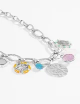 Collar plateado con cadena de eslabones grandes y dijes colgantes de diferentes formas y colores: medalla plateada texturizada, tortuga plateada con detalles turquesa, dije redondo rosa con brillos, dije redondo con borde de perlas, dije redondo con borde de cuentas amarillas y celeste, y cuenta cilíndrica azul.