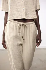 Pantalón de tiro alto color beige, con cintura elástica ajustable con cordones, bolsillos delanteros y pernera ancha.