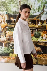 Blusa blanca de lino con cuello polo, manga larga y botones dorados. Presenta costuras a contratono en color naranja.