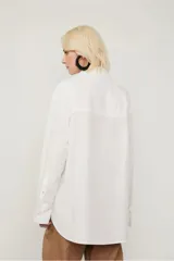 Camisa blanca amplia de algodón, con dos bolsillos en el frente, abotonada y con puños anchos.