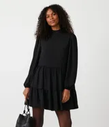 Vestido corto negro de chiffon con cuello alto, manga larga, volantes en la falda y cierre con botón en la espalda.