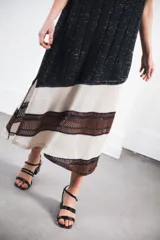 Vestido midi tejido en punto canalé negro con detalles en lurex plateado. Presenta calado artesanal en el ruedo, abertura lateral y etiqueta de cuero en la parte trasera del cuello.