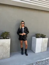 Chaqueta negra metalizada y acolchada, con cuello camisero, cierre frontal de botones y bolsillos de parche en el pecho.