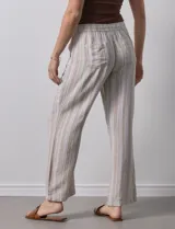 Pantalón de lino a rayas verticales color beige y blanco, con pretina ancha elastizada, lazo de ajuste y bolsillos inclinados.