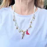 Collar corto hecho con cinta de tela blanca y dijes dorados, rojos y nacarados con forma de pez, corazón, coral, flor y cuentas.