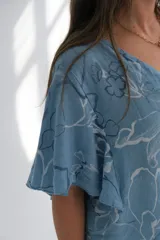 Blusa celeste con estampado de flores blancas y azules, de corte amplio y mangas cortas.