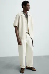 Camisa color marrón oscuro de corte relaxed fit, confeccionada en tejido de lino. Tiene cuello bowling, manga corta, bajo con aberturas laterales y cierre frontal de botonadura.