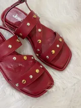 Sandalias rojas de cuero con tiras cruzadas y detalle de tachas plateadas y doradas.