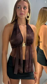Top halter de tela transparente con estampado marmolado en tonos marrón y beige. Presenta un escote pronunciado en V y se ajusta en la cintura con un fruncido central, donde se sujeta con un broche decorativo dorado con forma de caracol o concha marina.