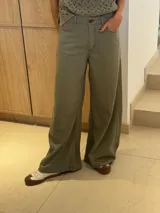 Pantalón ancho color verde oliva, de tiro alto y corte holgado. Confeccionado en mezcla de algodón y lino, con pinzas debajo de la rodilla, bordado de monograma en el bolsillo delantero y pespuntes a contratono.