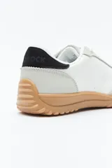 Zapatilla urbana de mujer con silueta retro, combinando paneles de gamuza marrón oscuro y material color crema en el cuerpo. Presenta detalles en color bordó en el talón y cordones beige. La suela es robusta de color marrón claro con relieve.