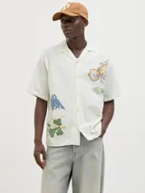 Camisa de algodón color crudo con estampado de flores y billetes, cuello resort, calce relajado, mangas cortas y cierre de botones.