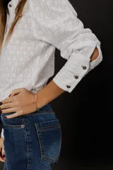 Camisa blanca de voile de algodón con bordado floral, corte clásico, cuello camisero y cierre frontal con botones. Mangas largas con puños abotonados.
