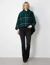 Capa corta de tejido grueso, color verde esmeralda con diseño de cuadros escoceses en azul marino y líneas finas en beige. Posee cuello alto que se cruza al frente y se cierra con un broche oscuro.