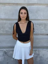 Top corto negro con lunares blancos, escote en V, mangas cortas con lazos en los hombros y corte ajustado.